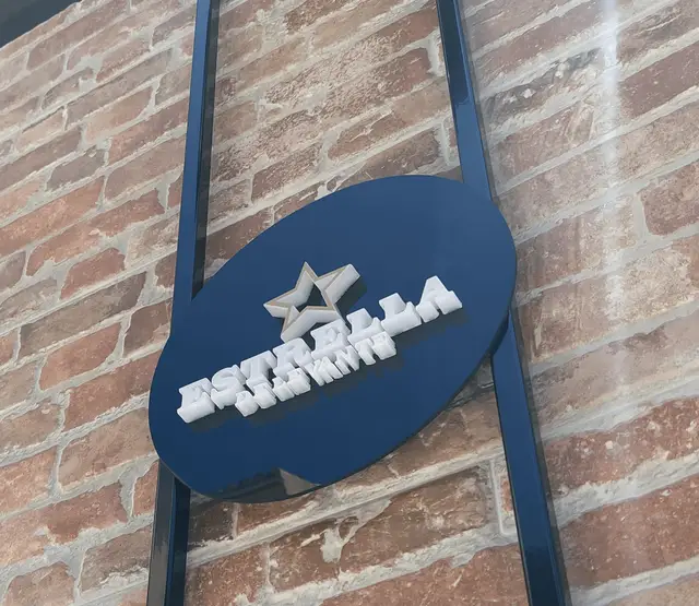 Letras recortadas de metacrilato blanco de 12 mm sobre panel de composite negro, La estrella lleva vinilo dorado en el frontal.